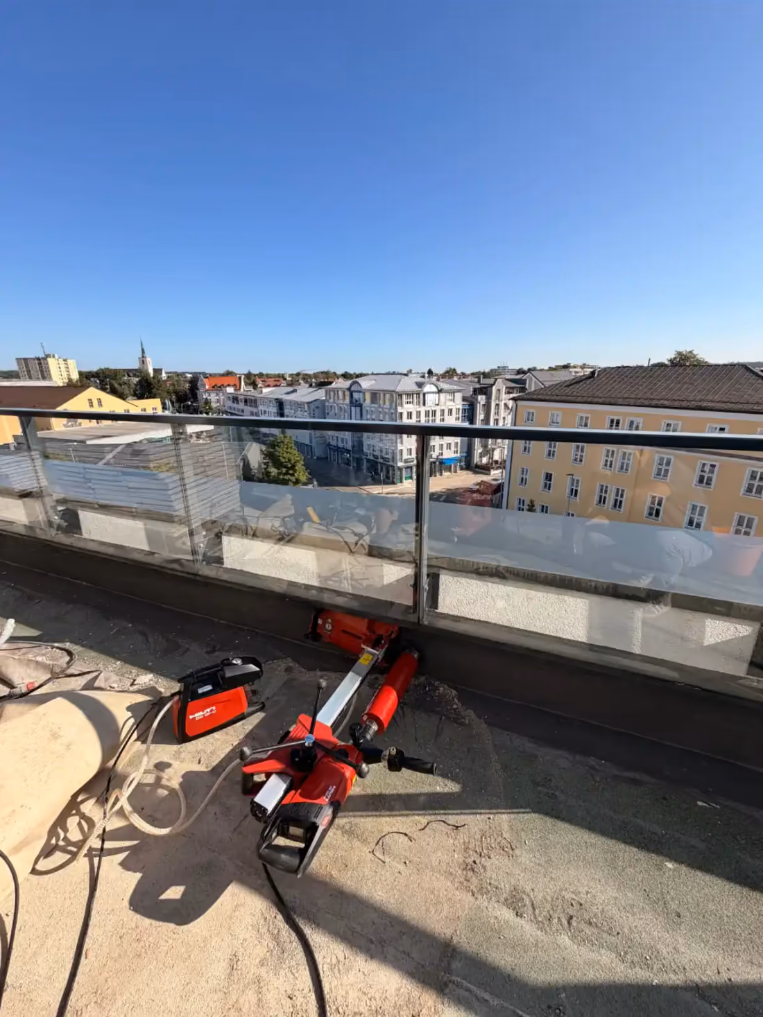 Kernbohrgerät auf einem Dach mit Glasgeländer, dahinter die Stadt