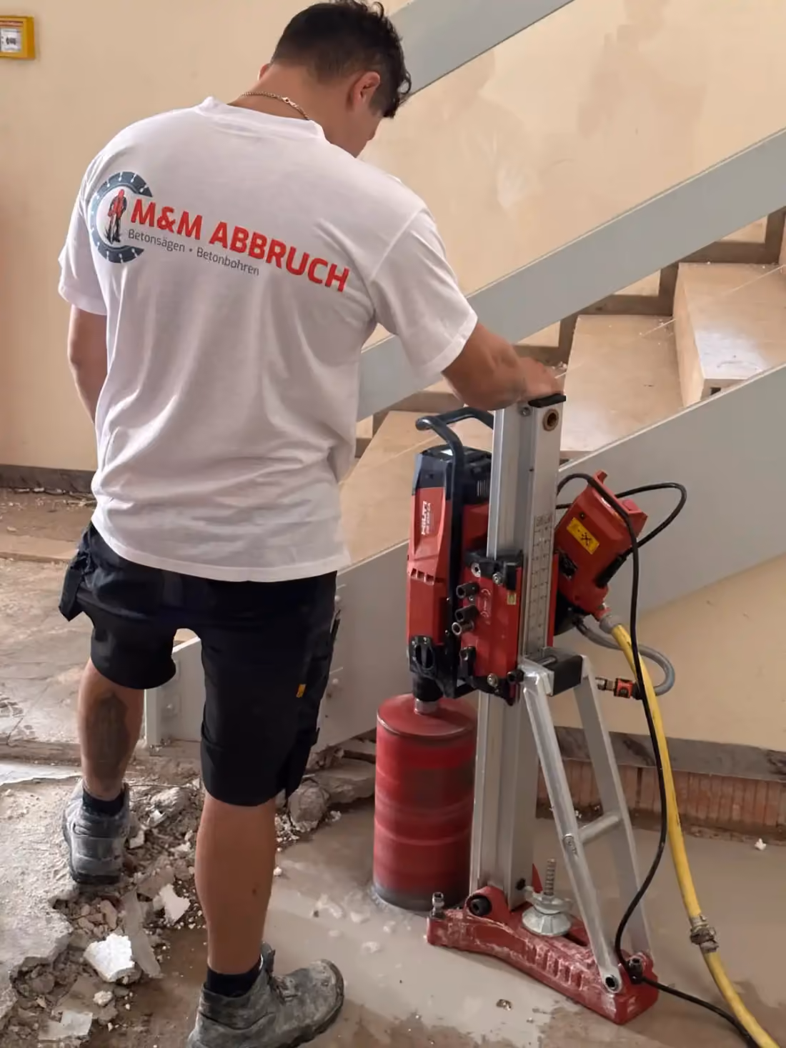 Mitarbeiter von M&M Abbruch mit Logo auf dem T-Shirt führt eine Kernbohrung auf einem Betonboden aus